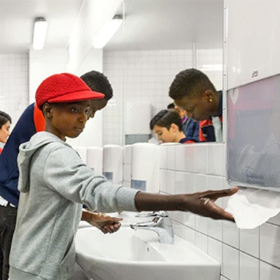 Unge drenge vasker hænder med Tork sæbe og tørrer hænder med Tork papir fra en hvid H2 dispenser
